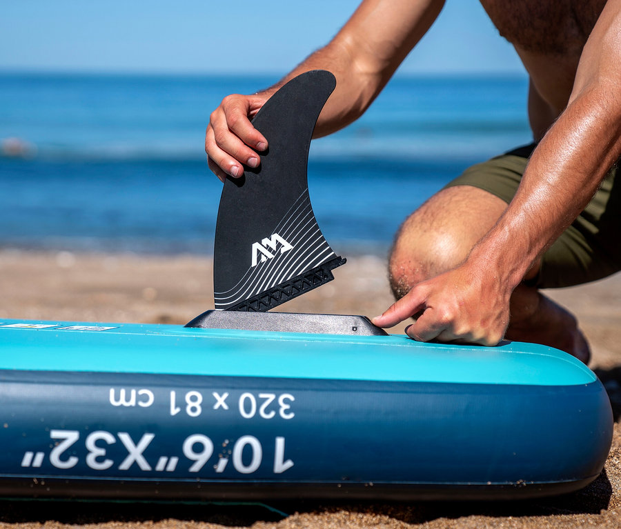 Mann befestigt eine Finne an einem Aqua Marina SUP Board »Beast« 10'6" am Strand.