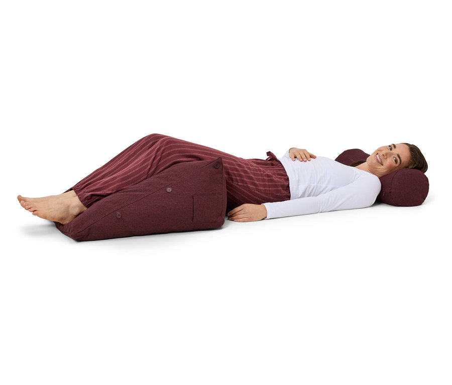 Eine Frau liegt auf dem Rücken auf einer Unterlage und hat Kissen unter ihren Füßen und ihrem Kopf.