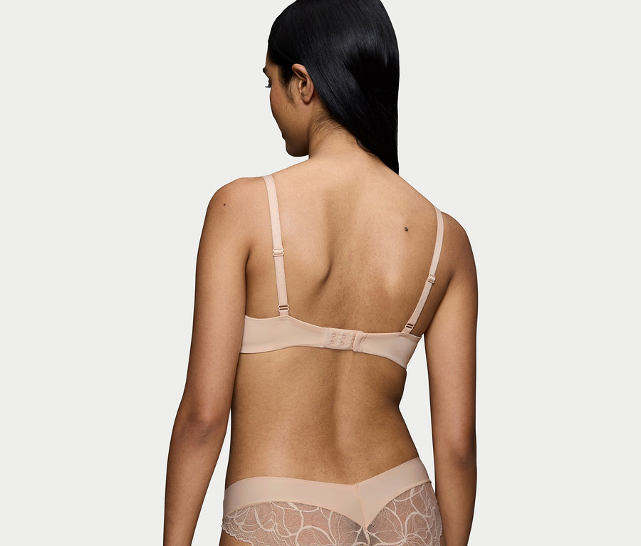 Rückansicht einer Frau mit schwarzen Haaren, die einen hautfarbenen BH und Slip mit Spitze trägt.