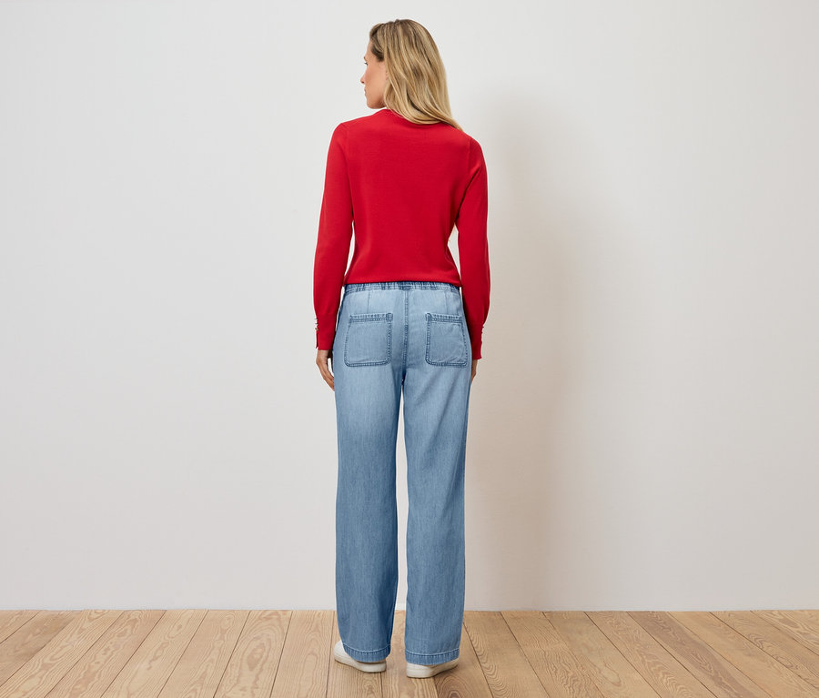 Eine Frau steht mit dem Rücken zur Kamera und trägt einen roten Pullover und blaue Jeans.