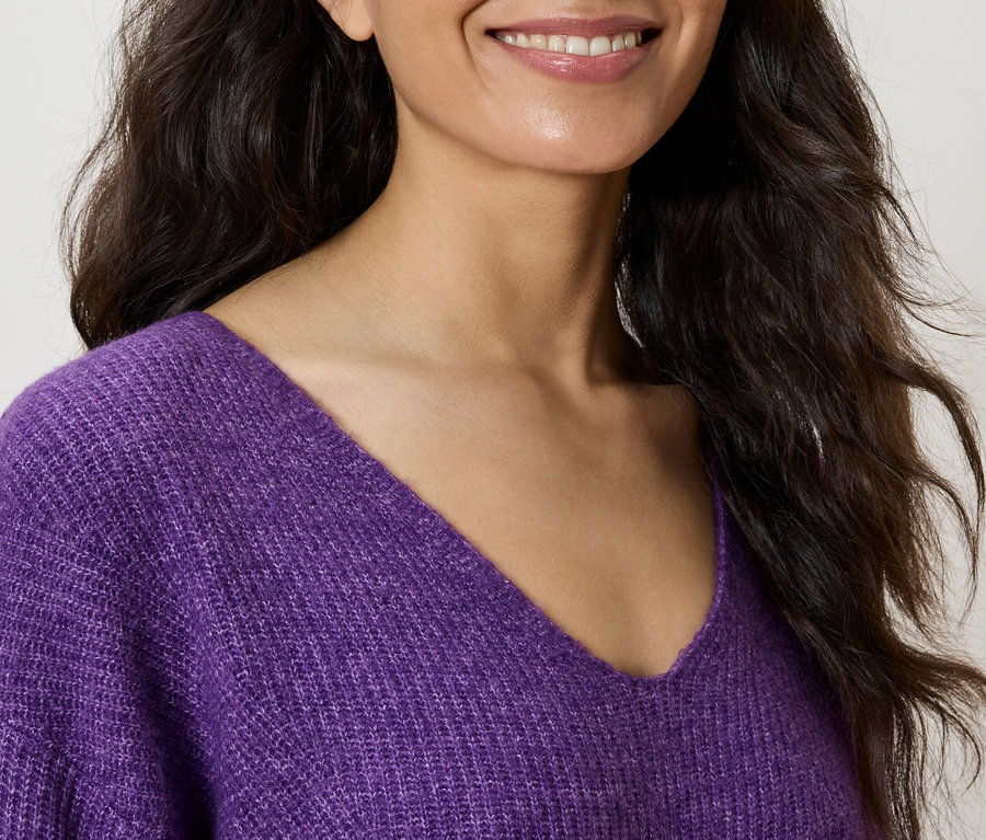 Lächelnde Frau trägt einen violetten Pullover mit V-Ausschnitt.