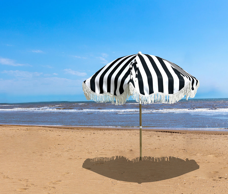 Ein Leco Strand-Sonnenschirm mit schwarzen und weißen Streifen und Fransen steht am Strand.