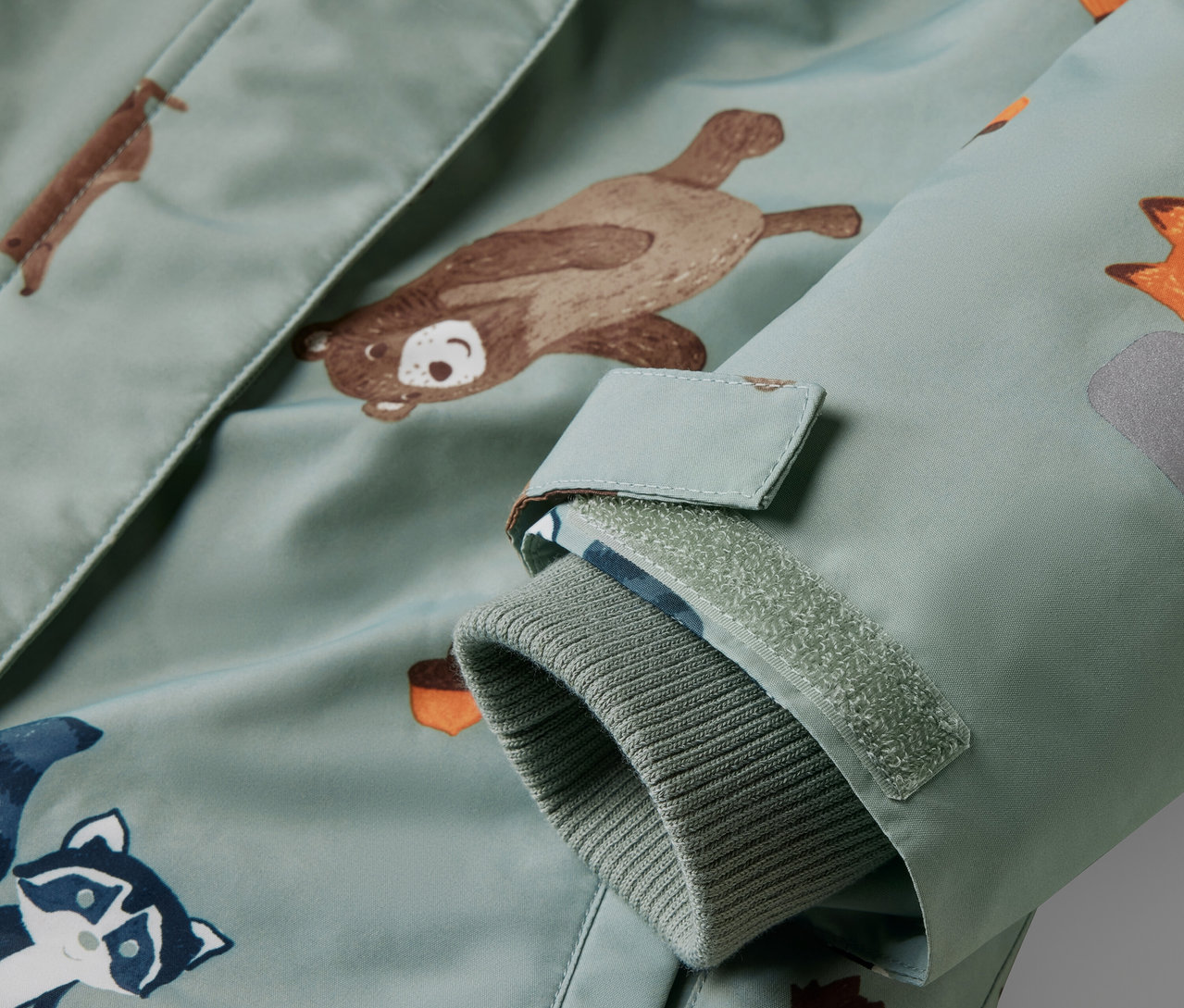 Detailansicht eines Kinder-Schneeanzugs mit Tiermuster und Klettverschluss.