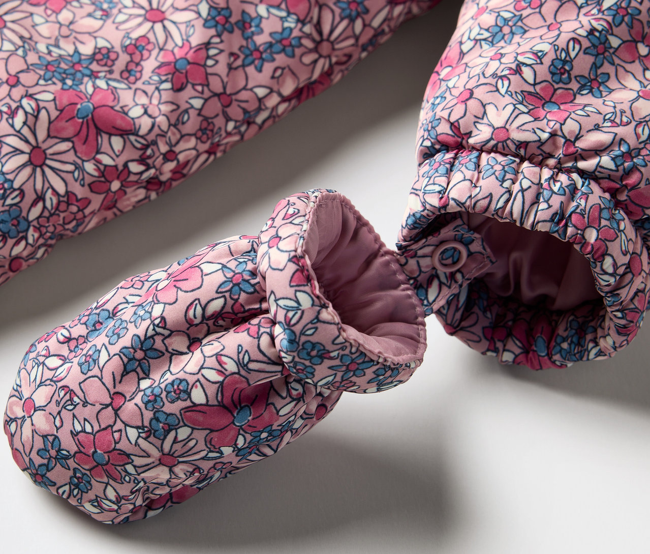 Detailansicht eines Baby-Winteroveralls mit Blumenmuster und Handschuh.