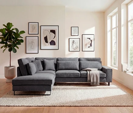 Wohnzimmer mit grauem Ecksofa, Kissen, Decke, Zimmerpflanze und sechs gerahmten Kunstdrucken an der Wand über einem beige Teppich.