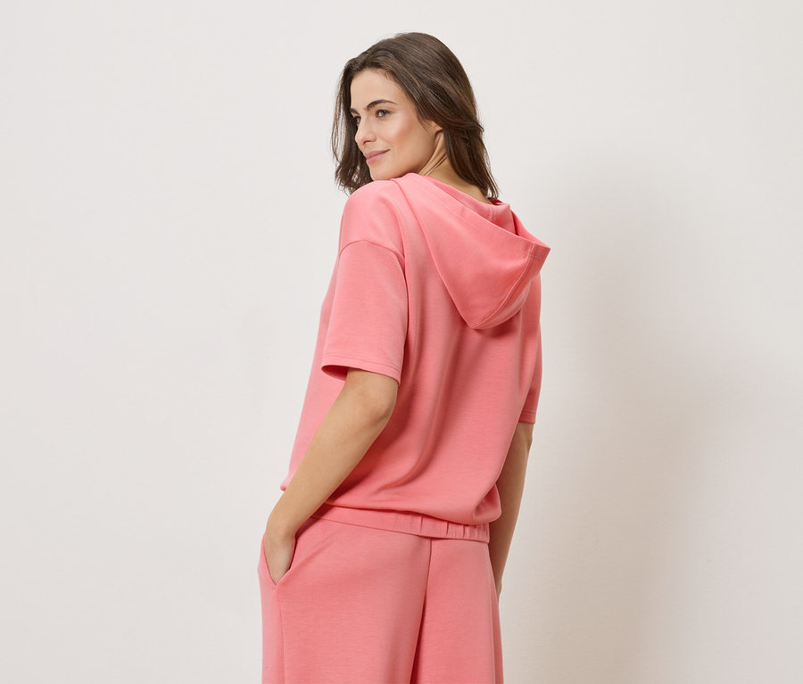 Frau trägt einen korallenroten Short-Sleeve-Hoodie und passende korallenrote Shorts.