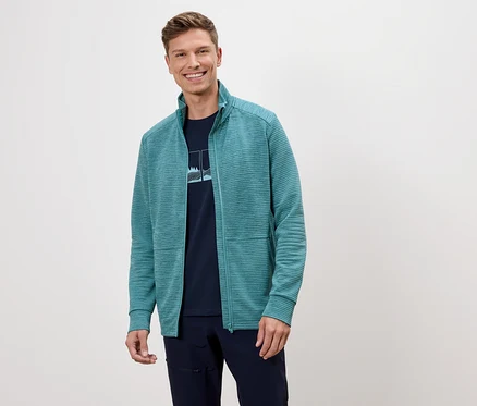 Ein Mann lächelt und trägt eine türkisfarbene Fleecejacke über einem marineblauen T-Shirt.