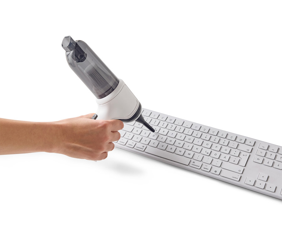 Eine Hand benutzt einen Mini-Staubsauger, um eine weiße Computertastatur zu reinigen.
