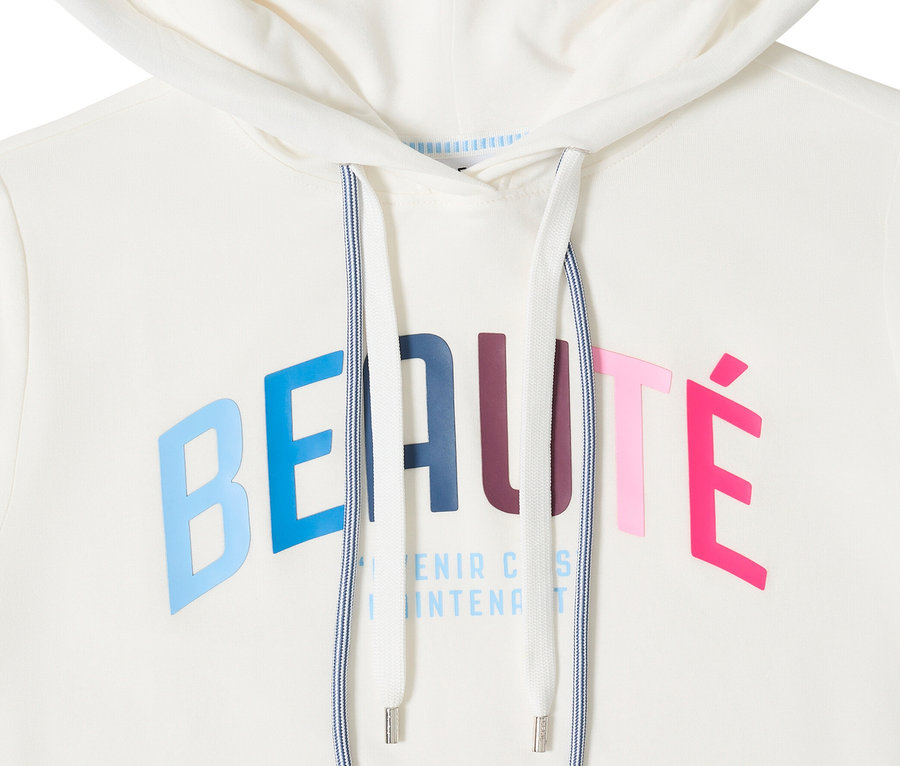 Nahaufnahme des CECIL Hoodie-Shirts in Weiß mit Kapuze und Kordelzug. Der Schriftzug "Beauté" ist in bunten Buchstaben aufgedruckt.