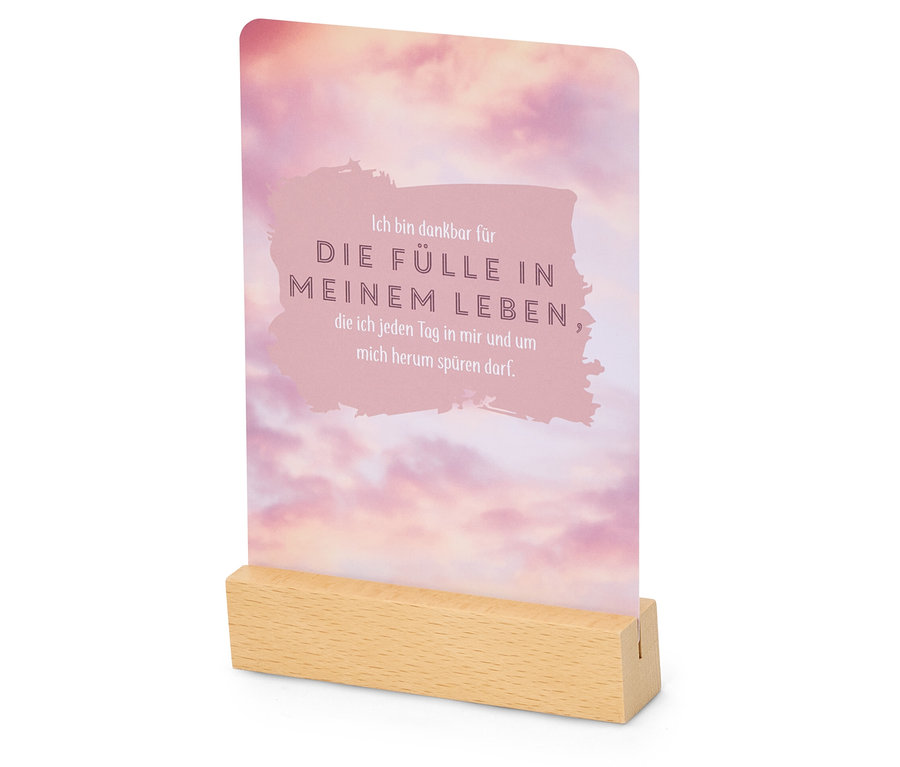 Karte mit rosa Wolkenmuster und der Aufschrift "Ich bin dankbar für die Fülle in meinem Leben" in einem Holzständer.