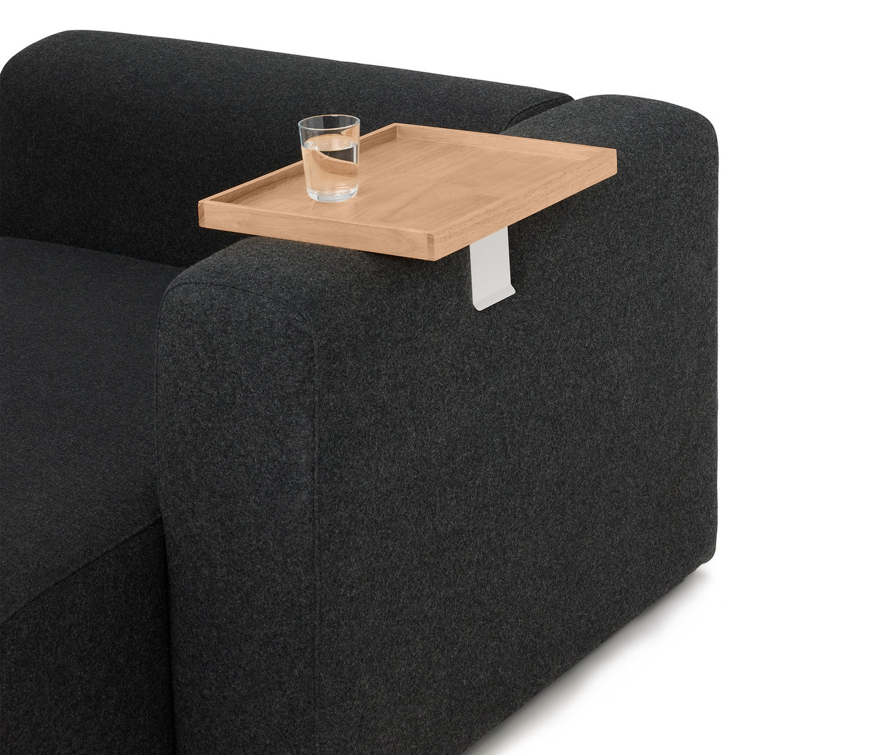 Auf der Armlehne eines grauen Sofas steht ein Holztablett mit einem Glas Wasser.