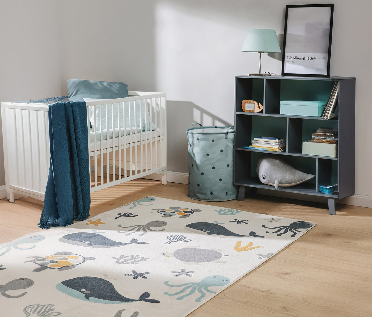 Ein Kinderzimmer mit einem weißen Gitterbett, einem grauen Regal und einem Teppich mit Meeresmotiven.