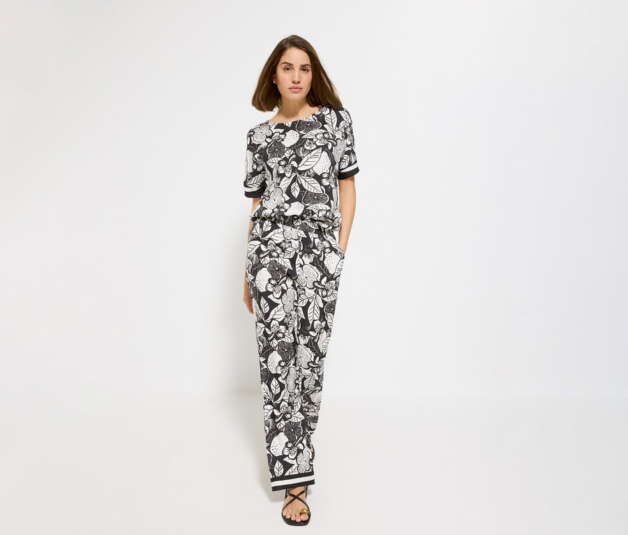 Frau mit floralem Oberteil und Olsen Wide Leg Hose. Sie trägt schwarze Sandalen.