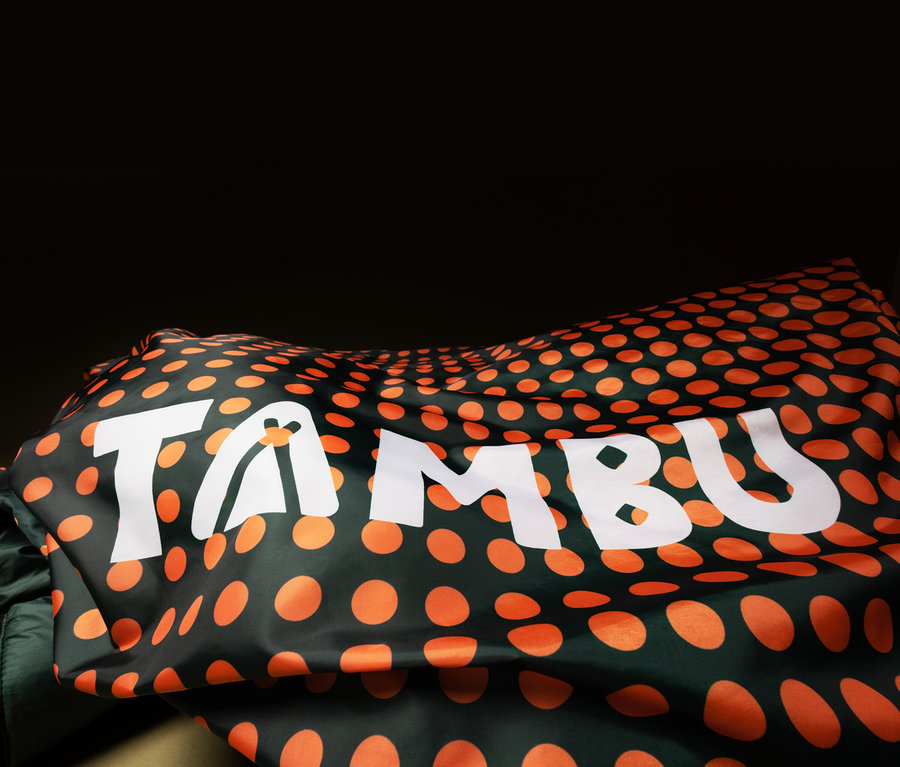 Stoff mit orangenen Punkten und dem weißen Schriftzug "TAMBU" liegt auf einem Gegenstand.