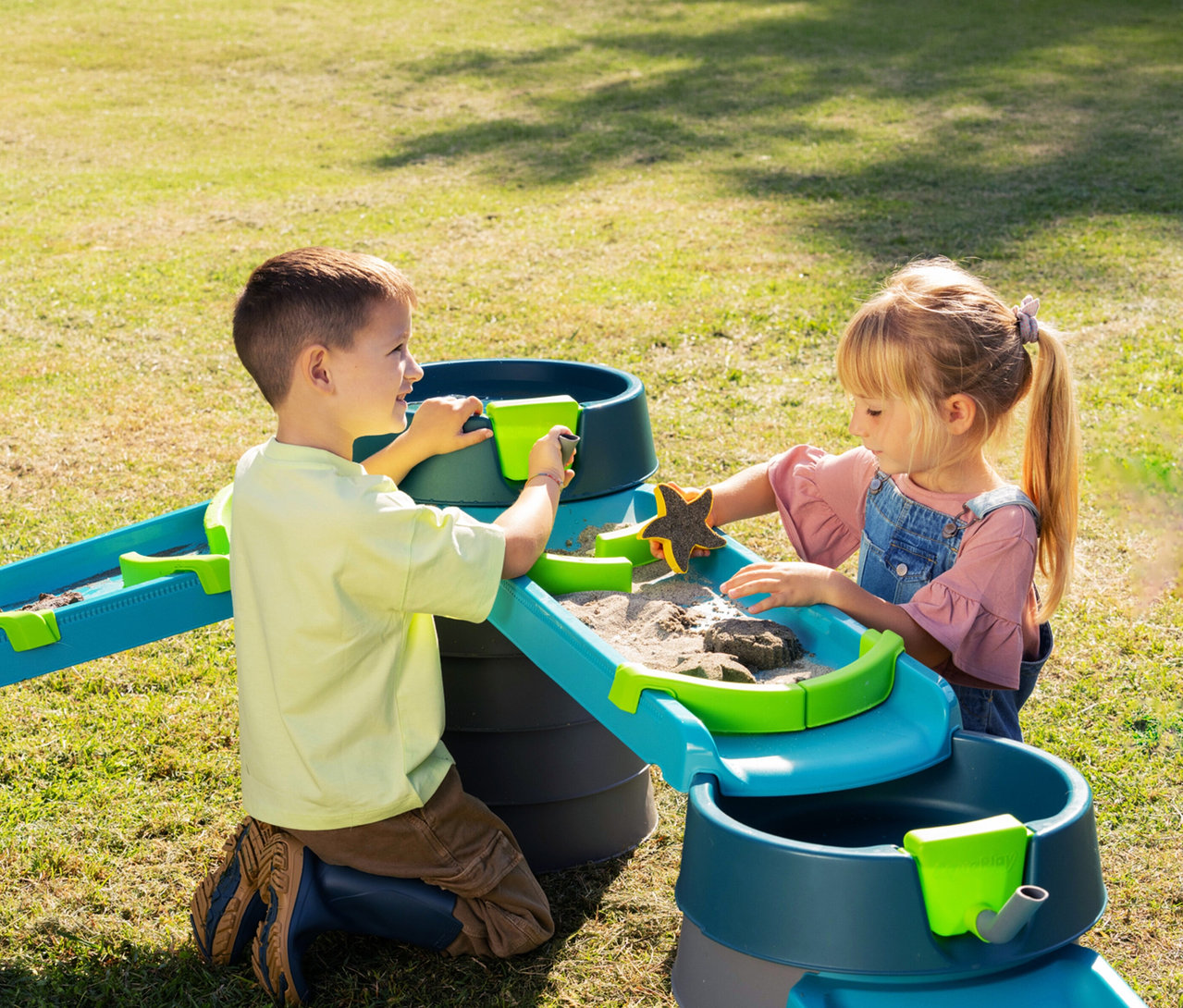 Zwei Kinder spielen mit der AquaPlay »Mudway STREAM« Matschbahn im Garten.