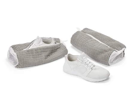 Ein weißer Turnschuh vor einem grauen Schuhbeutel. Ein weiterer Schuh steckt in einem offenen Beutel, ein dritter Beutel ist geschlossen.