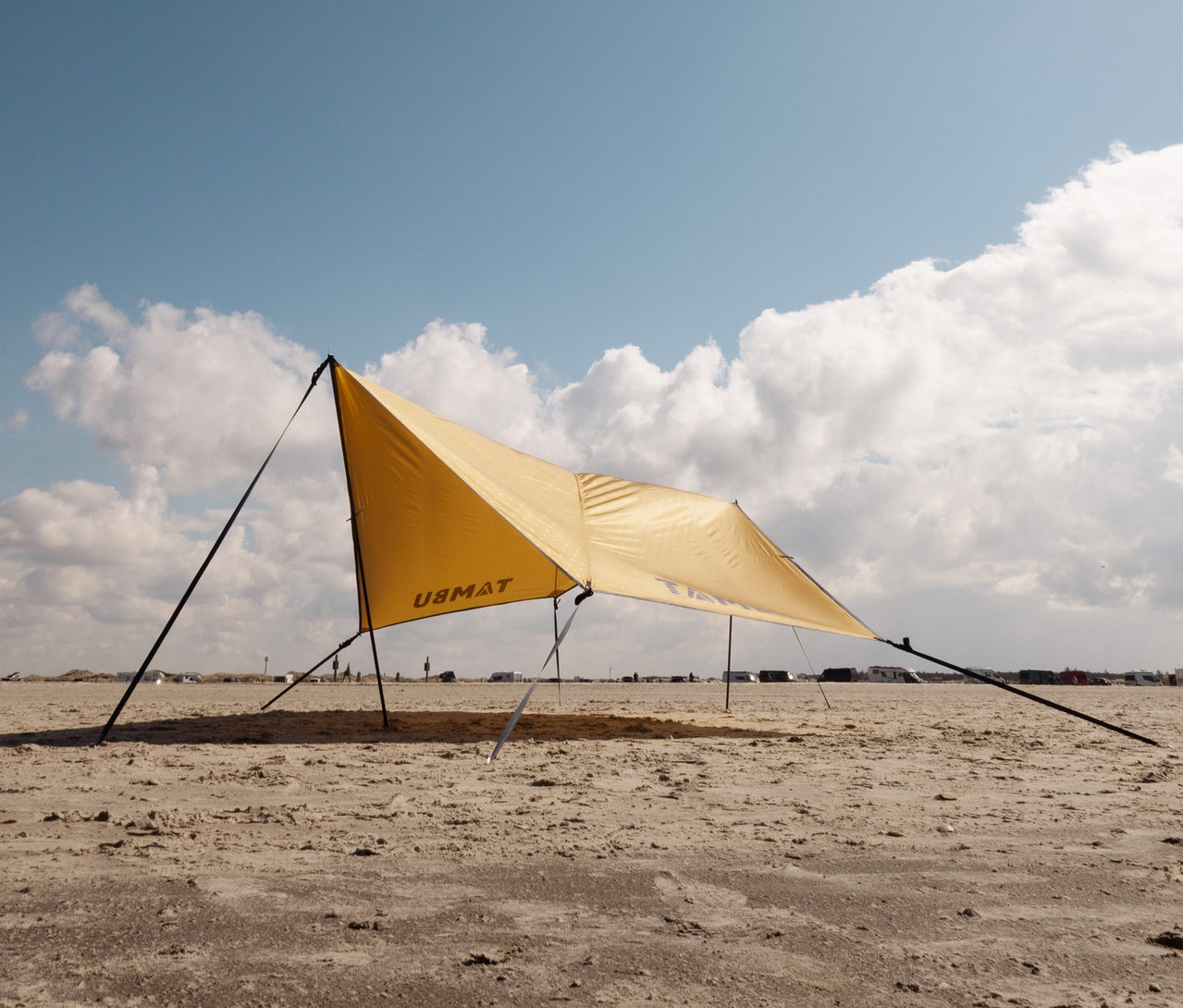 Gelbes Tambu »PALA« Tarp/Sonnensegel steht am Strand unter bewölktem Himmel.