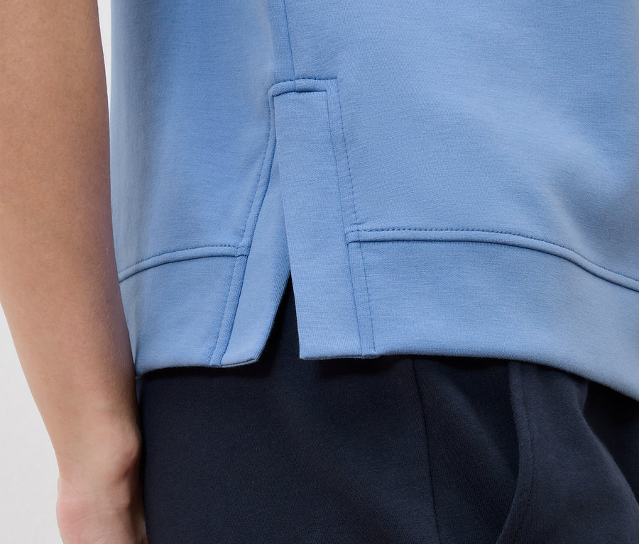 Detailansicht eines hellblauen Sweatshirts mit Seitenschlitz über einer marineblauen Hose.