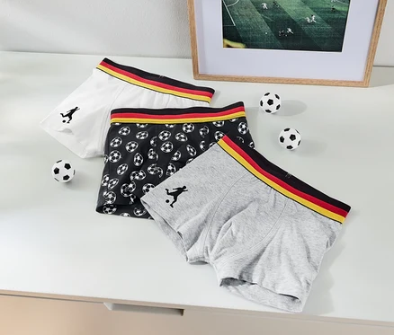 Drei Boxershorts liegen auf einem Tisch, eine weiße, eine graue und eine schwarze mit Fußballmuster.