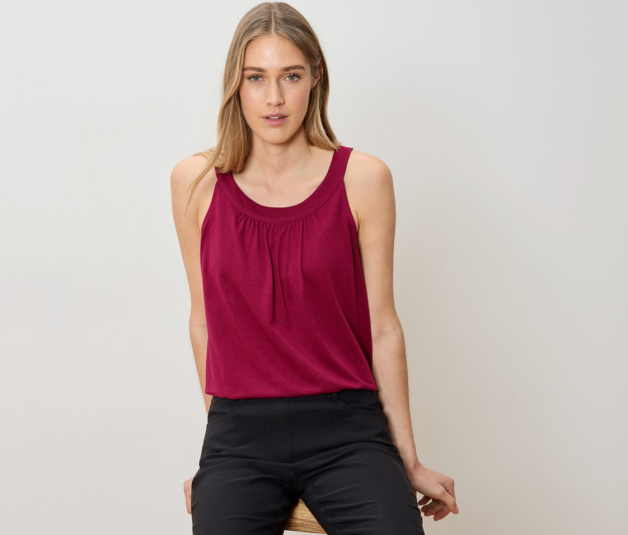 Frau sitzt und trägt ein ärmelloses Top und eine schwarze Hose.