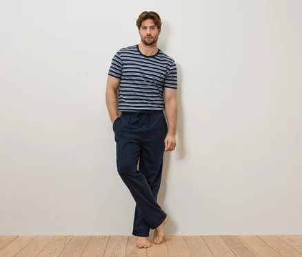 Mann lehnt an einer Wand, trägt ein blau-weiß gestreiftes T-Shirt und eine marineblaue Pyjamahose.