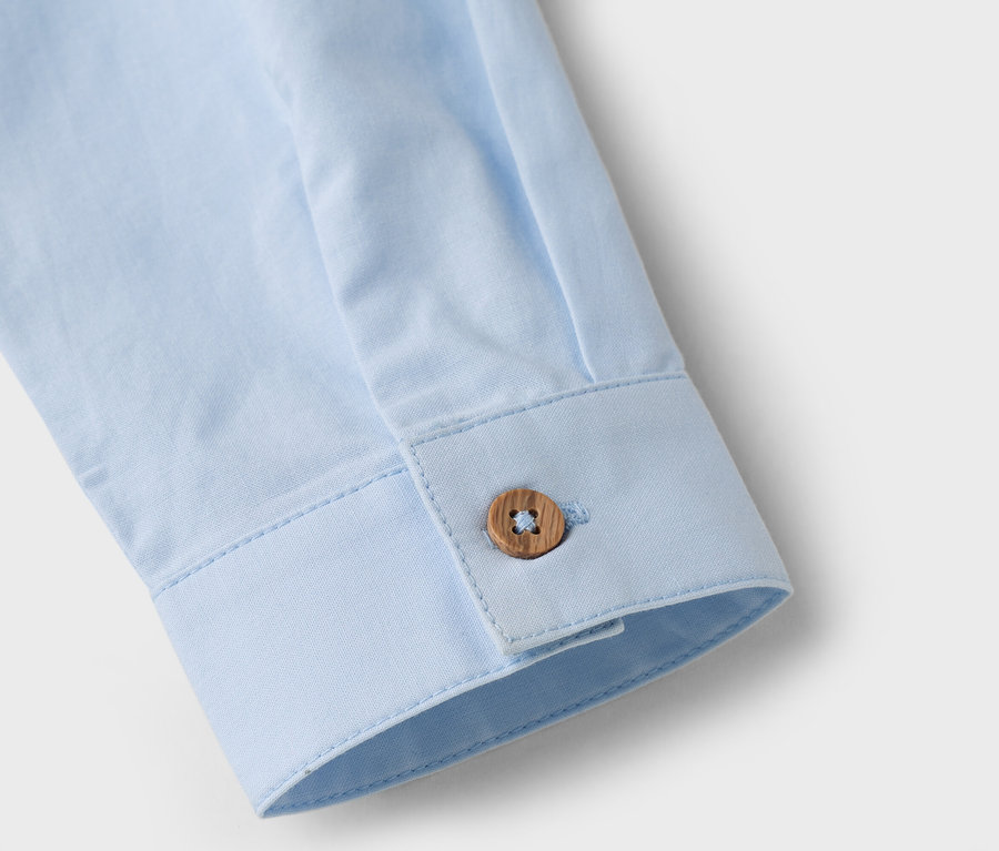 Nahaufnahme vom Ärmel eines hellblauen Hemdes mit einem braunen Knopf.