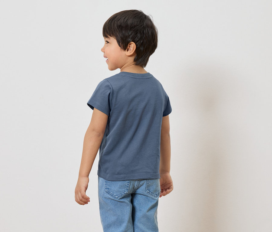 Rückansicht eines Jungen mit dunklen Haaren, der ein blaues T-Shirt und Jeans trägt.
