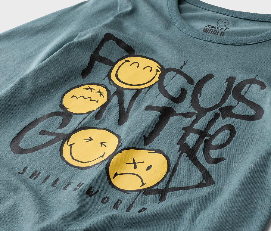 Nahaufnahme eines petrolfarbenen Smiley World Langarmshirts mit dem Aufdruck "Focus on the Good" und gelben Smileys.