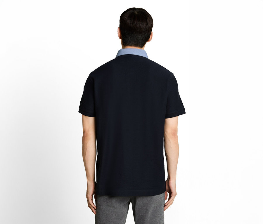 Rückenansicht einer Person in einem dunkelblauen, kurzärmeligen Poloshirt mit hellblauem Kragen und grauer Hose.