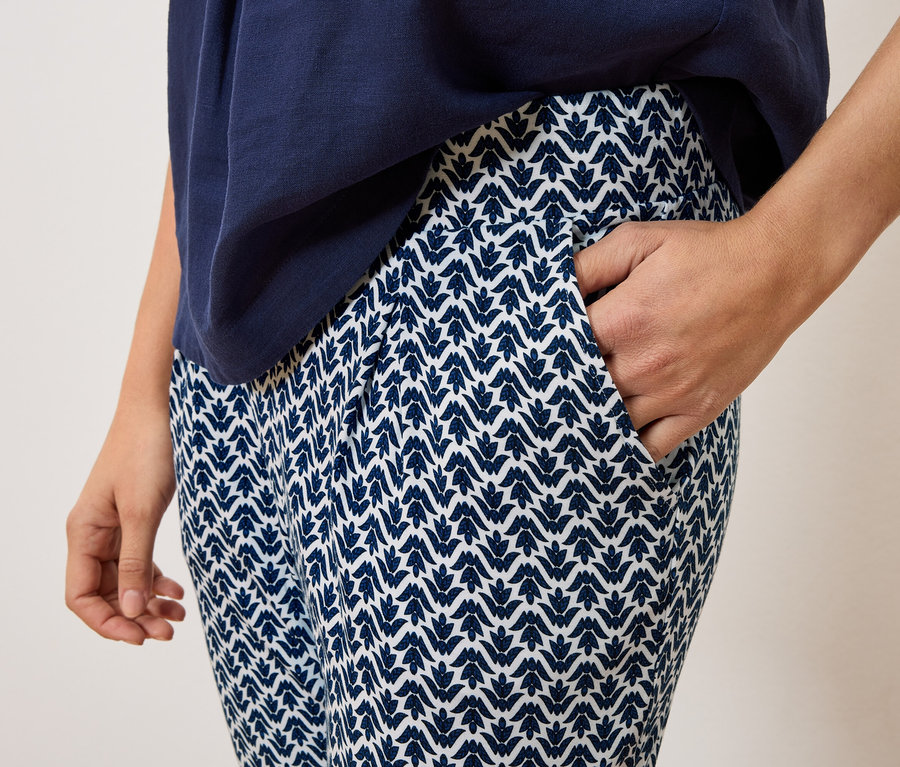 Nahaufnahme einer Person, die eine marineblaue Hose mit weißem Muster und ein marineblaues Oberteil trägt, wobei eine Hand in der Hosentasche steckt.