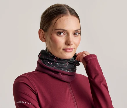 Frau in bordeauxrotem Langarmshirt und schwarzem Halstuch mit Blumenmuster, das Halstuch mit der Hand zurechtziehend.