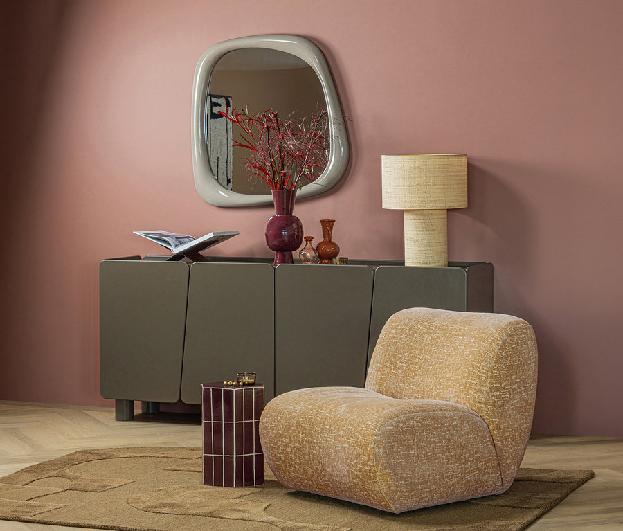Ein Raum mit rosa Wand, dunkelgrauem Sideboard, unregelmäßigem Spiegel und beiger Lampe. Ein beiger Sessel und ein kleiner roter Beistelltisch stehen auf einem braunen WOOOD Teppich »Livo«.