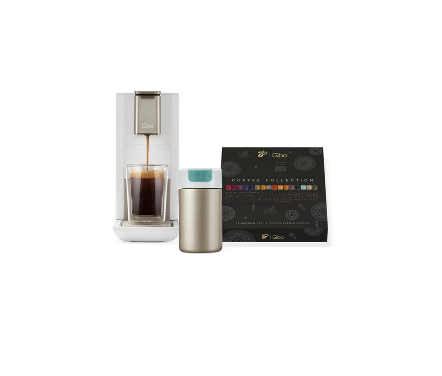 Weißer Qbo Kaffeeautomat brüht Kaffee in ein Glas, daneben eine goldene Kambukka Thermotasse und eine schwarze Qbo Coffee Collection Kapselbox. Goldenes Bundle.