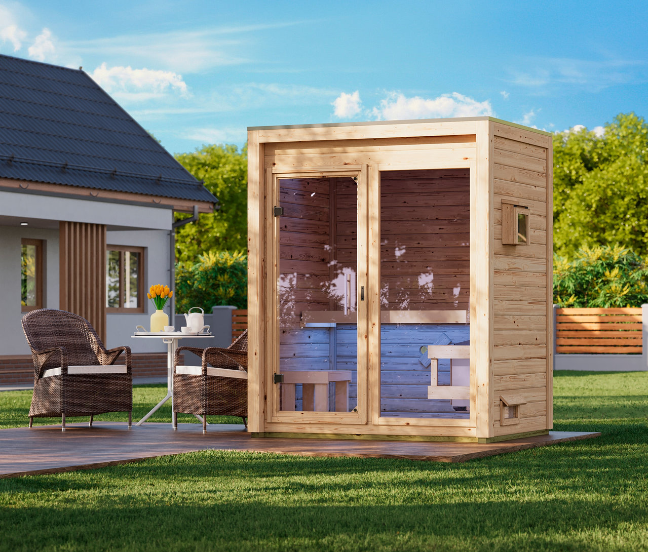 Eine hölzerne Außensaunakabine mit Glastür steht auf einer Holzterrasse in einem grünen Garten. Daneben befinden sich zwei Korbsessel und ein kleiner weißer Tisch mit gelben Blumen auf der Terrasse. Im Hintergrund sind ein modernes Haus und Bäume unter blauem Himmel zu sehen.