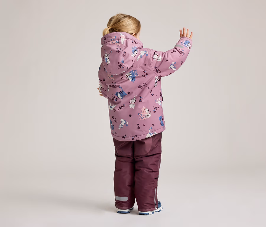 Ein Kind von hinten in einer lila Jacke mit Katzenmuster und einer lila Hose, die eine Hand hebt.