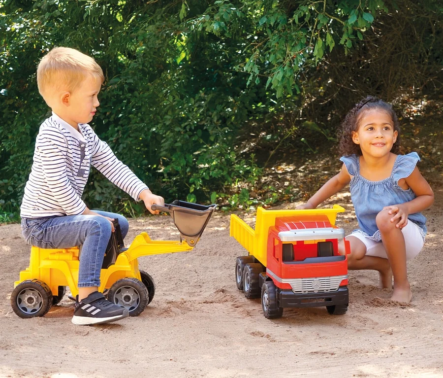 Junge sitzt auf gelbem Spielzeugbagger, Mädchen hockt neben rotem und gelbem GIGA TRUCKS Muldenkipper »Actros« im Sand.