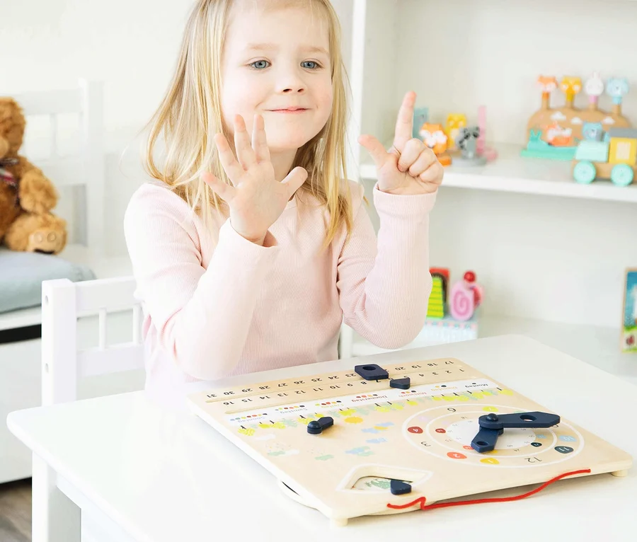 Mädchen zeigt mit Fingern die Zahl Sieben an einer hölzernen Lernuhr mit Kalender »Educate«.
