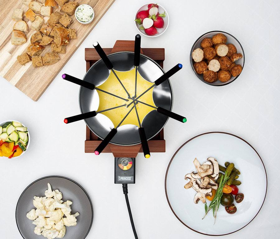 Fondue-Set mit Brot, Gemüse und Fleischbällchen auf einem weißen Tisch.