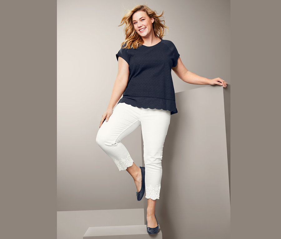 Frau posiert in Blusenshirt mit Lochstickerei und 7/8-Jeans.