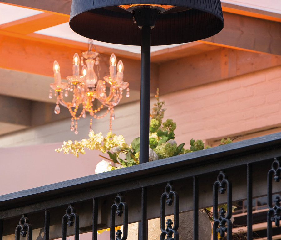 Ein schwarzer Sunred-Stand-Heizstrahler »Halogen Artix Basic« steht auf einer Terrasse mit einem Kristalllüster im Hintergrund.