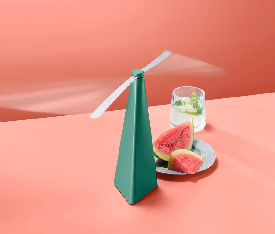 Ein grüner Fliegenwedler steht neben einem Glas Wasser und einer Wassermelone.