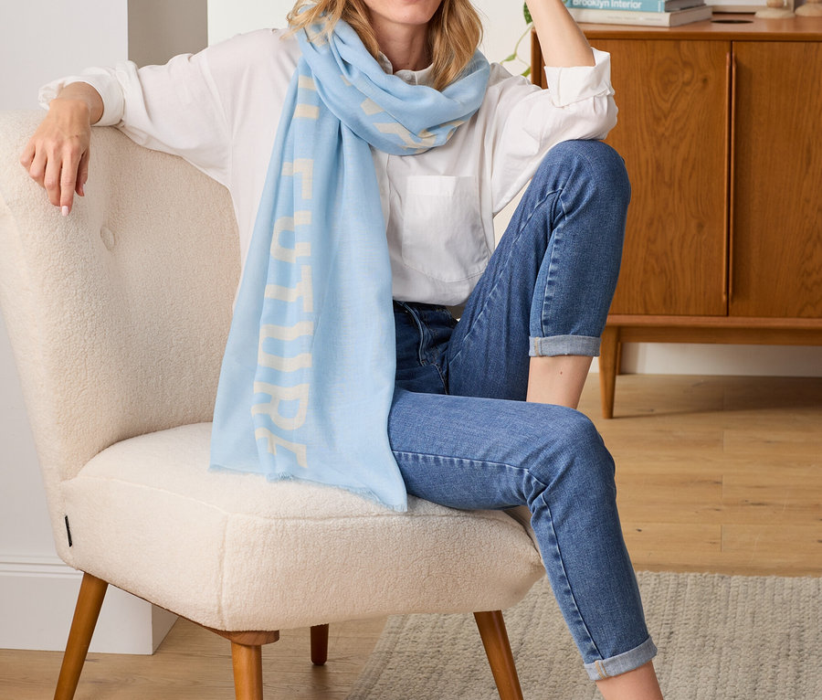 Frau sitzt im Sessel und trägt einen Webschal mit Statement-Print.