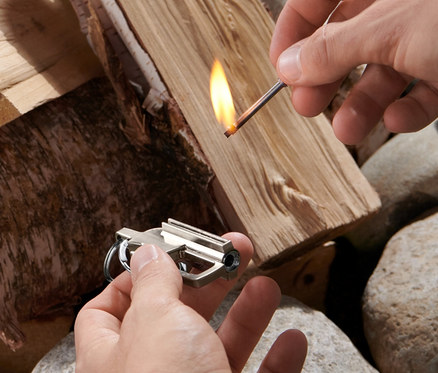 Mann zündet mit einem Streichholz Holz für ein Feuer an und hält einen Camping-Feuerstarter in der Hand.