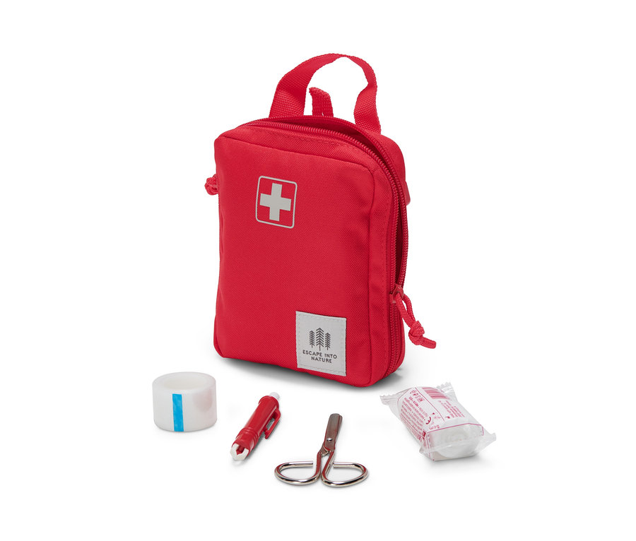 Eine rote Erste-Hilfe-Tasche mit Pflaster, Schere und Verband liegt auf einem weißen Hintergrund.