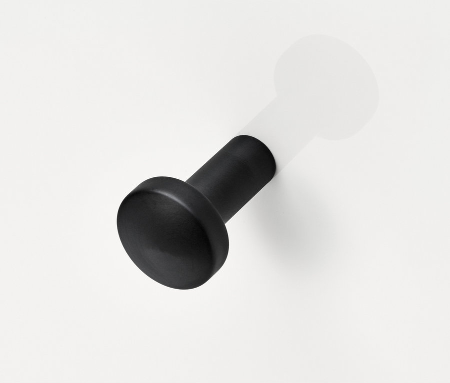 Schwarzer Holzhaken an einer weißen Wand.