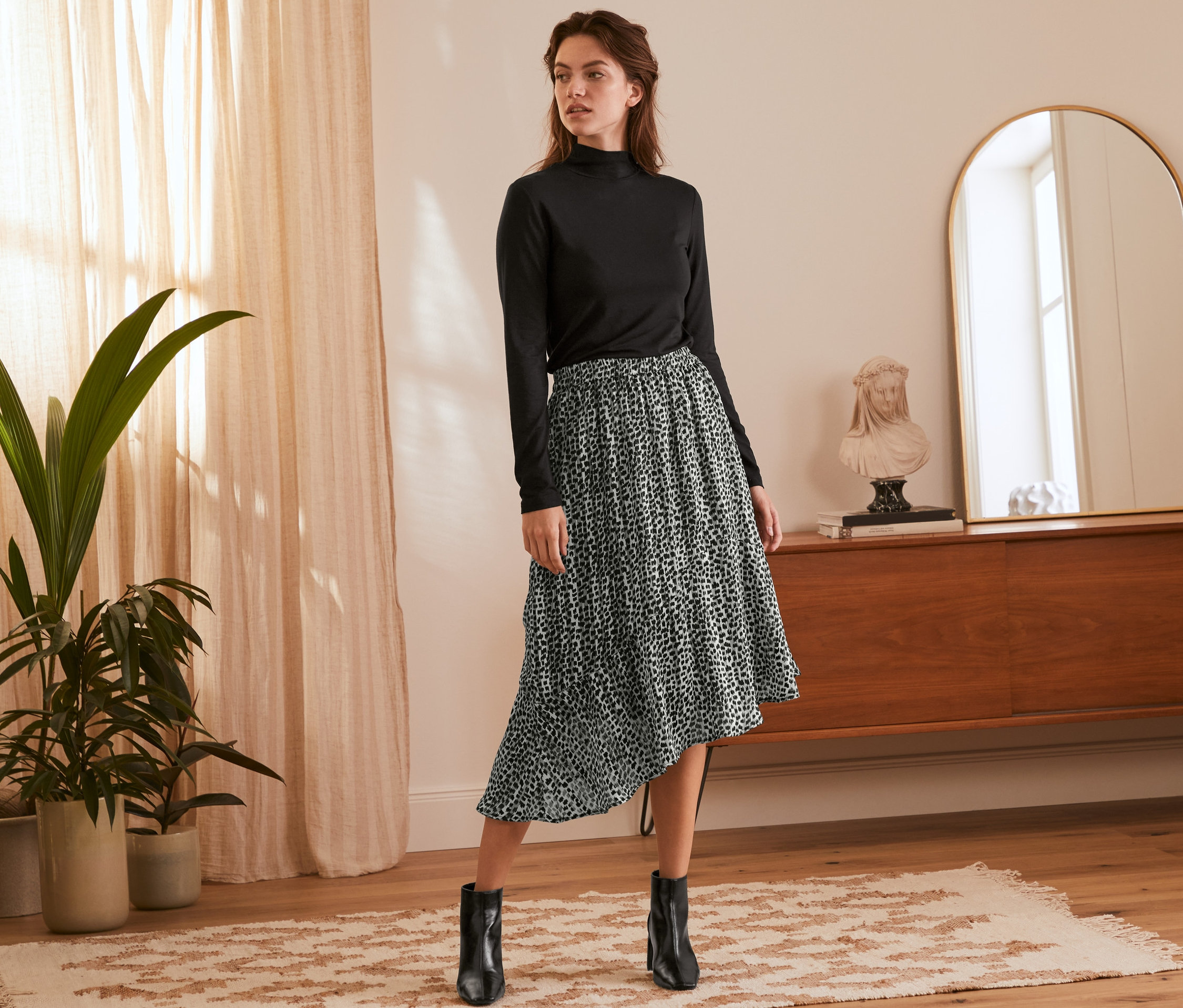 Frau posiert in schwarzem Rollkragenpullover und asymmetrischem Rock mit Animal-Print.