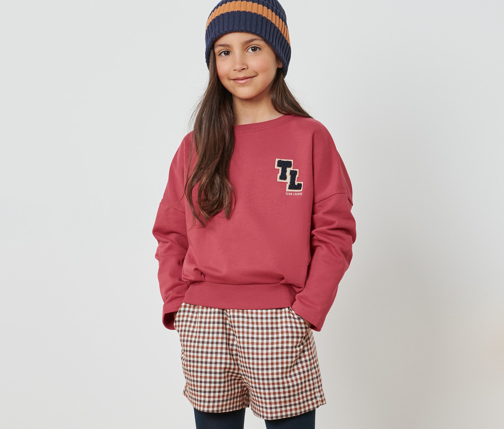 Mädchen in Sweater, karierten Shorts, Leggings und Stiefeln.