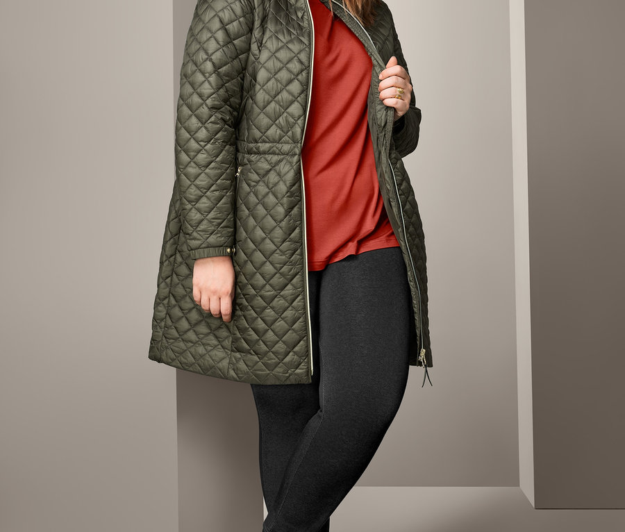 Frau posiert in olivgrüner Steppjacke, rotem Oversized-Shirt und gefütterten Leggings in Jeansoptik.