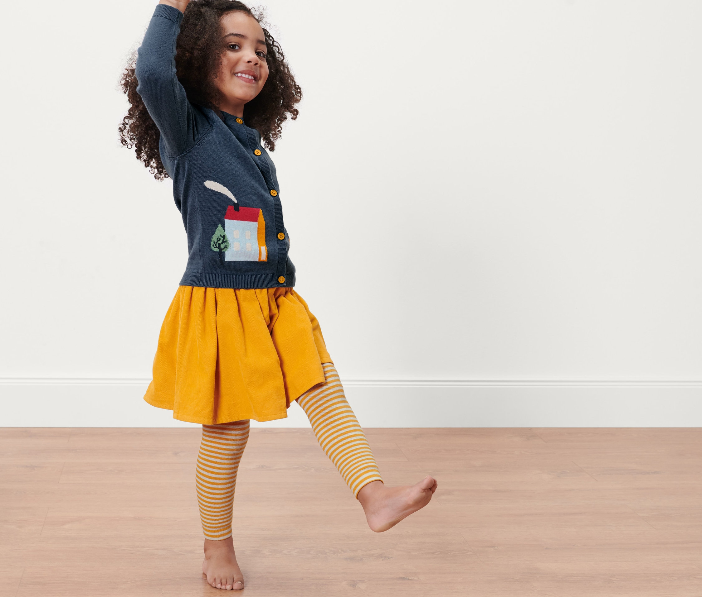 Mädchen posiert mit 3 Kinder-Thermoleggings, Streifen, gelbem Rock und blauem Cardigan.