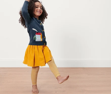 Mädchen posiert mit 3 Kinder-Thermoleggings, Streifen, gelbem Rock und blauem Cardigan.